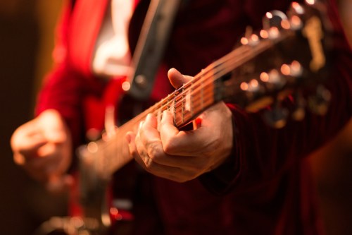 A close-up of a musician's hand playing an electric guitar, with a blurred background.