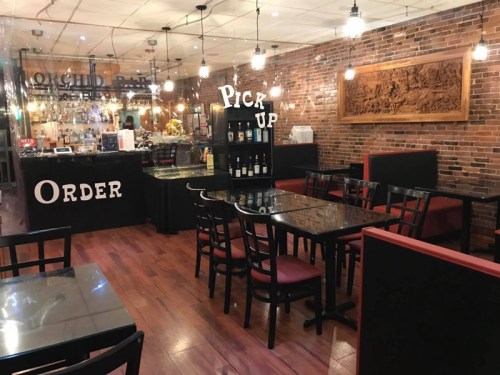 Interior of a restaurant featuring brick walls, tables, and a bar area with signs for "Order" and "Pick Up."