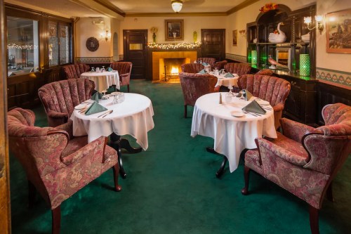 Cozy restaurant interior with elegant tables, plush chairs, and a warm fireplace, decorated for a festive atmosphere.