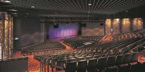 A spacious theater interior with rows of empty seats and a colorful stage backdrop, ready for a performance.