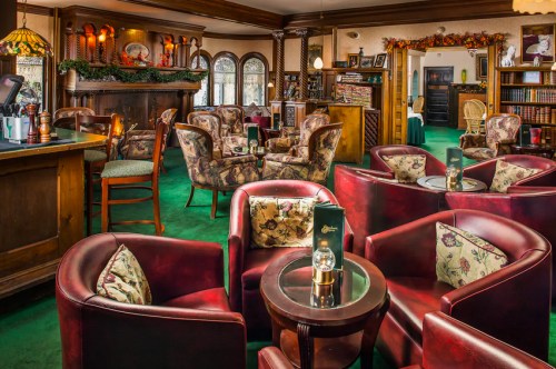 Cozy lounge with plush armchairs, a bar, and warm lighting, featuring green carpet and decorative autumn accents.