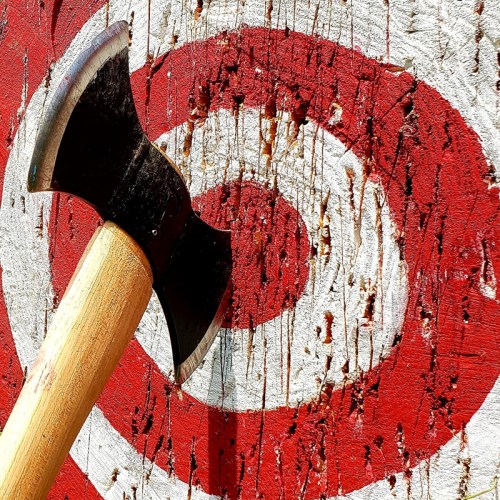 A close-up of an axe embedded in a wooden target with red and white concentric circles.