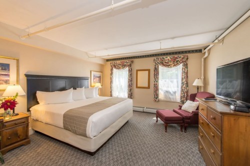 Cozy hotel room featuring a king bed, armchair, dresser, and large windows with patterned curtains.