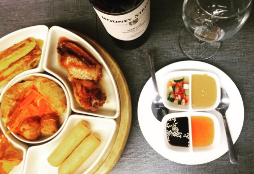 A platter of assorted appetizers with dipping sauces, accompanied by a bottle of wine and a glass.