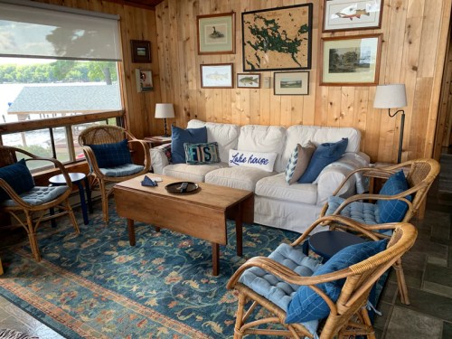Cozy living room with a white sofa, wooden coffee table, rattan chairs, and nautical decor on wooden walls.