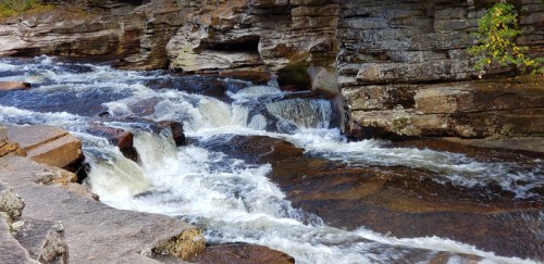 A flowing river cascades over rocks, surrounded by rugged stone formations and greenery.