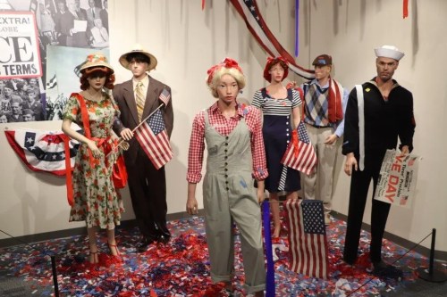 A display of mannequins in vintage clothing, holding American flags, set against a patriotic backdrop.