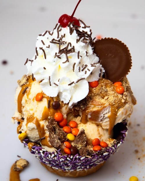 A colorful ice cream sundae topped with whipped cream, a cherry, chocolate sprinkles, and a peanut butter cup.