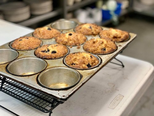 A tray of freshly baked muffins with a few missing, resting on a wire rack in a kitchen setting.