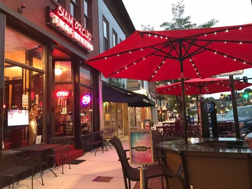 Outdoor dining area with red umbrellas at Siam Orchid restaurant, illuminated by evening lights.