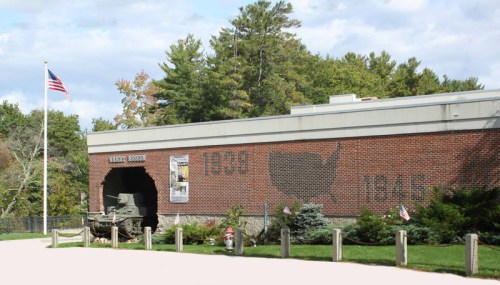 Exterior view of a museum featuring a tank, with a mural of the U.S. outline and the years 1939 and 1945. American flag visible.