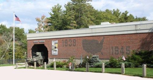 Exterior view of a brick building with a military tank, flags, and a mural featuring the year 1945 and a map of the USA.