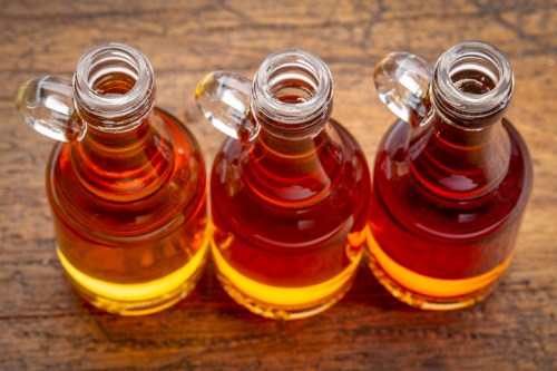 Three glass bottles with liquid in shades of amber and yellow, placed on a wooden surface.