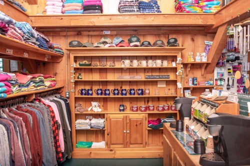 A cozy shop interior featuring shelves of clothing, hats, and mugs, with wooden accents and a warm atmosphere.