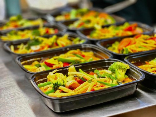 Several meal prep containers filled with colorful stir-fried vegetables and sauce, arranged on a stainless steel surface.