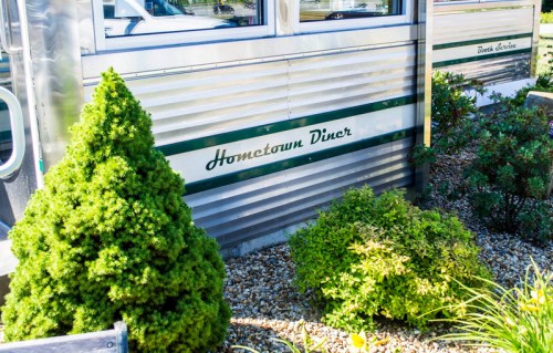 Exterior of Hometown Diner with shiny metal siding and green shrubs in front.
