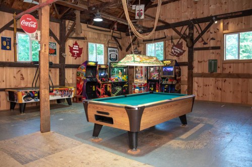 A rustic game room featuring a pool table, arcade machines, and wooden walls with various decorations.