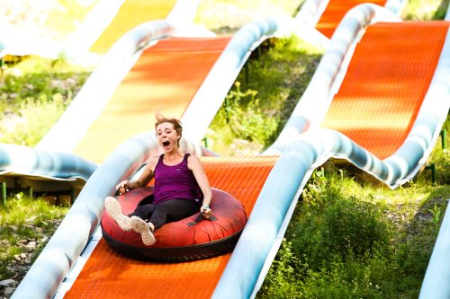 A woman joyfully slides down a colorful inflatable tube on a water slide surrounded by greenery.