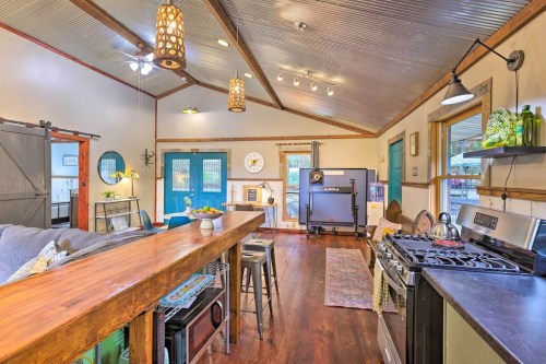 Cozy kitchen and living area with wooden bar, modern appliances, and rustic decor, featuring bright natural light.