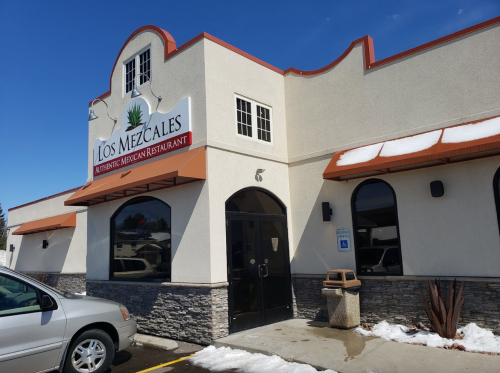 Exterior of Los Mezcales, an authentic Mexican restaurant, featuring a sign and a clear blue sky. Snow on the ground.