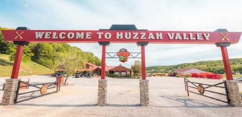 Welcome sign for Huzzah Valley, featuring a rustic archway and surrounding greenery.