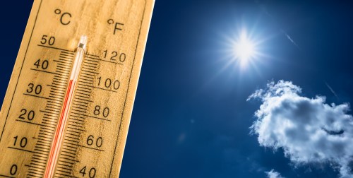 A thermometer shows high temperatures against a bright blue sky with the sun and a few clouds.