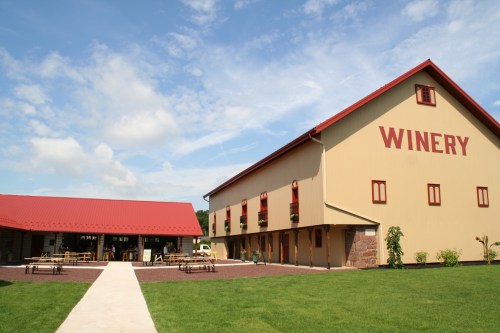 A large winery building with a red roof and "WINERY" painted on the side, surrounded by green grass and blue skies.
