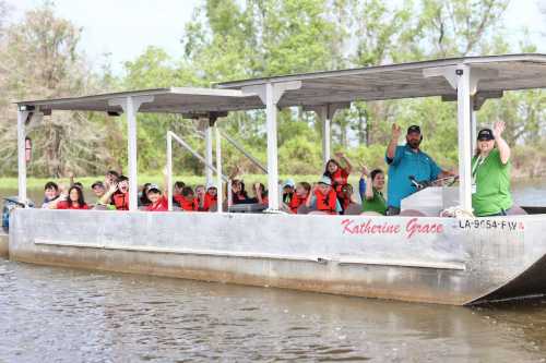 A group of people in life jackets wave from a boat on a river, surrounded by greenery.