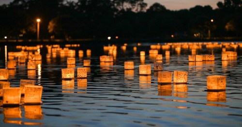 Floating lanterns illuminate a calm lake at dusk, creating a serene and reflective atmosphere.