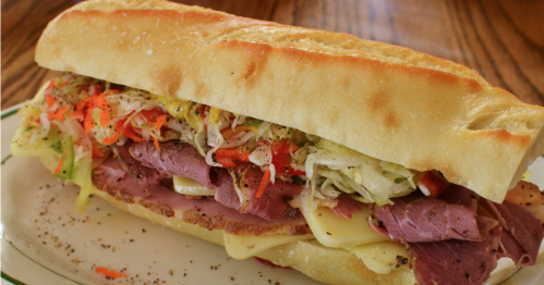 A hearty sandwich on a crusty roll, filled with layers of deli meats, cheese, and colorful shredded vegetables.