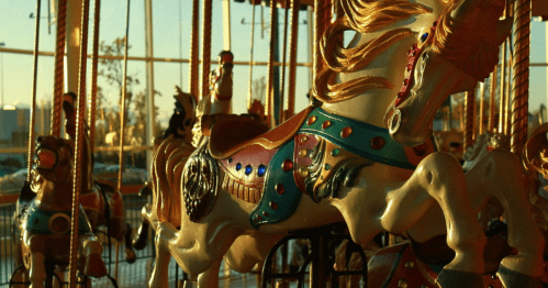 A close-up of colorful carousel horses, illuminated by warm sunlight, with a blurred background of more horses.