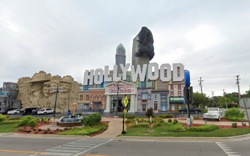 A large "HOLLYWOOD" sign in front of a themed building featuring a war museum and a giant King Kong statue.
