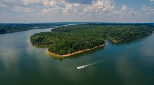 Aerial view of a lush green island surrounded by calm water and blue skies with scattered clouds.