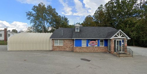 A brick building with a sign reading "Grill" and a large metal structure beside it, set against a cloudy sky.