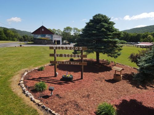 Sign for Wildwood RV Resort surrounded by landscaped flowers and trees, with a building and mountains in the background.