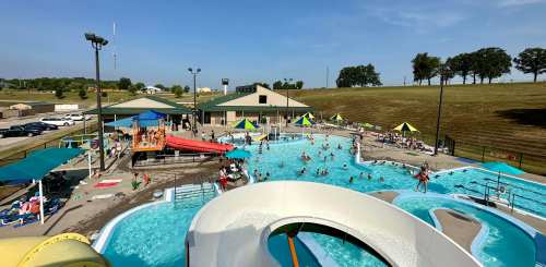 Aerial view of a busy water park with a pool, slides, and people enjoying the sun on a clear day.