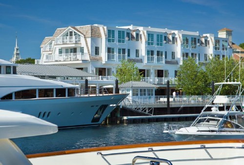A marina scene featuring luxury yachts and a modern waterfront building under a clear blue sky.