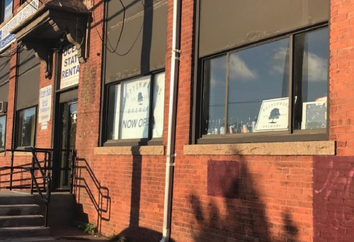 A brick building with large windows displaying "Now Open" signs and bottles visible inside.