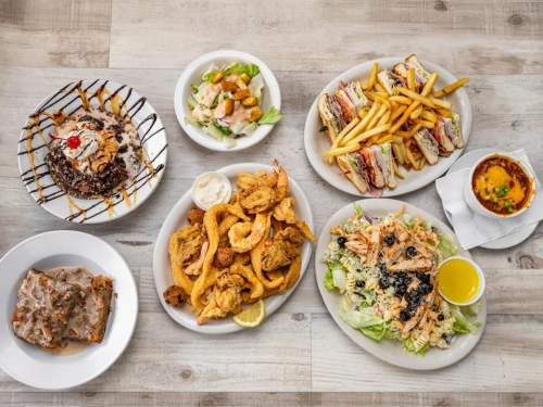 A spread of various dishes including salads, sandwiches, fried seafood, fries, and desserts on a wooden table.