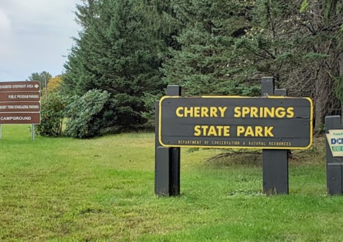 Sign for Cherry Springs State Park, surrounded by trees, with additional signs for parking and campground information.