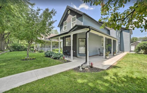 A charming blue house with a porch, surrounded by greenery and a well-maintained lawn on a sunny day.