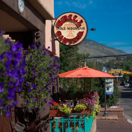 A vibrant outdoor dining area with colorful flowers and a sign for "Grill Cantina" against a scenic mountain backdrop.