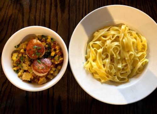 A bowl of scallops with corn and vegetables next to a plate of fettuccine pasta.
