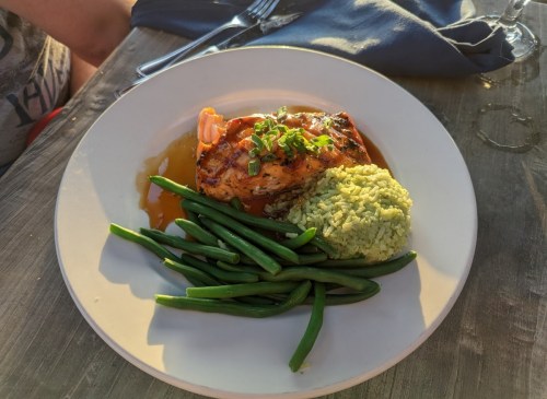 Grilled salmon with green beans and a side of herb rice on a white plate, served on a wooden table.