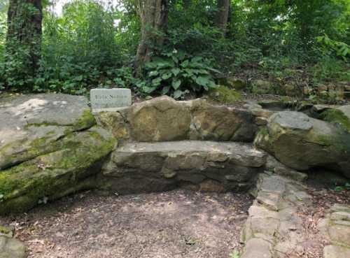 A stone seating area surrounded by greenery, featuring a plaque that reads "Bella Nevin Memorial."