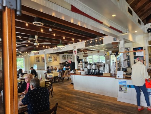 A cozy restaurant interior with wooden beams, patrons dining, and a coffee bar in the background.