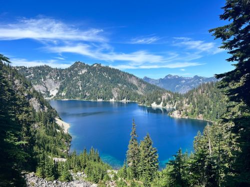 A serene lake surrounded by lush green trees and mountains under a clear blue sky.