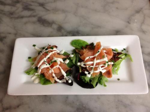 Two small plates of salad topped with smoked salmon, drizzled with mayonnaise, on a white rectangular dish.