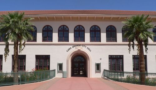 Front view of Casa Grande City Hall, featuring a light-colored building with arched windows and palm trees.