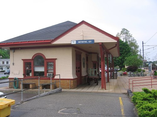 Historic train station in Mystic, CT, featuring a light-colored building with red trim and a sign above the entrance.